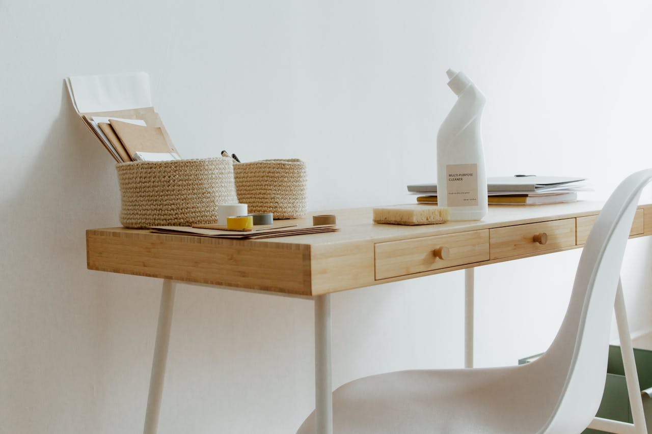 gallery-6 A clean and organized home office desk with cleaning products, papers, and storage baskets.