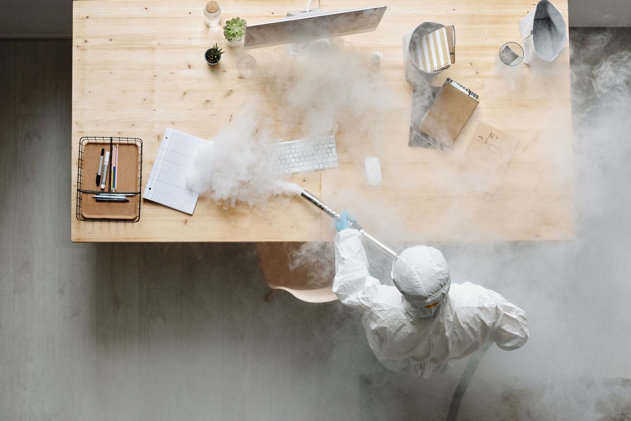 hero-img-01 An individual disinfects a workspace using fumigation, wearing full protective gear for safety.