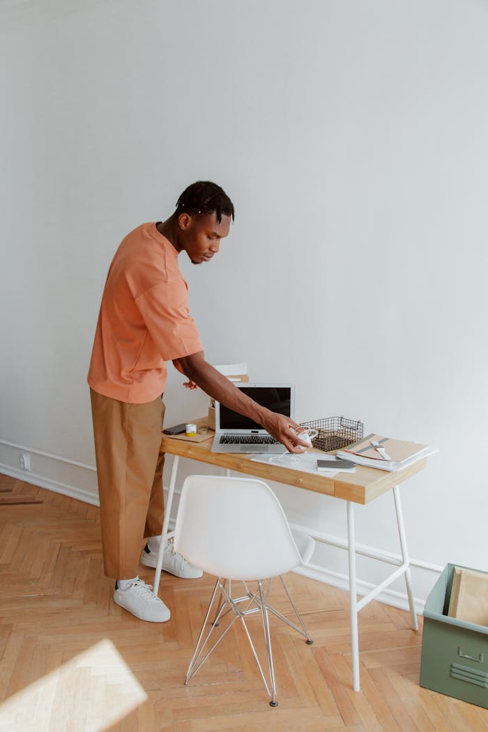 about-01 A man standing at a desk organizing papers and electronic devices in a modern office setting.